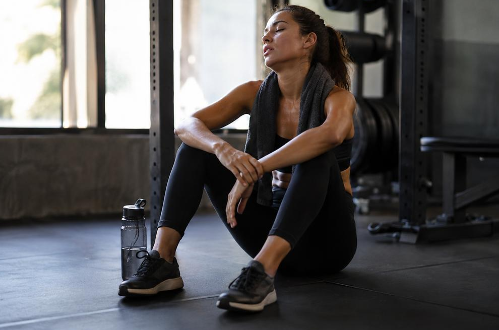 Woman resting on a gym bench after an intense workout, showing signs of fatigue and the need for recovery